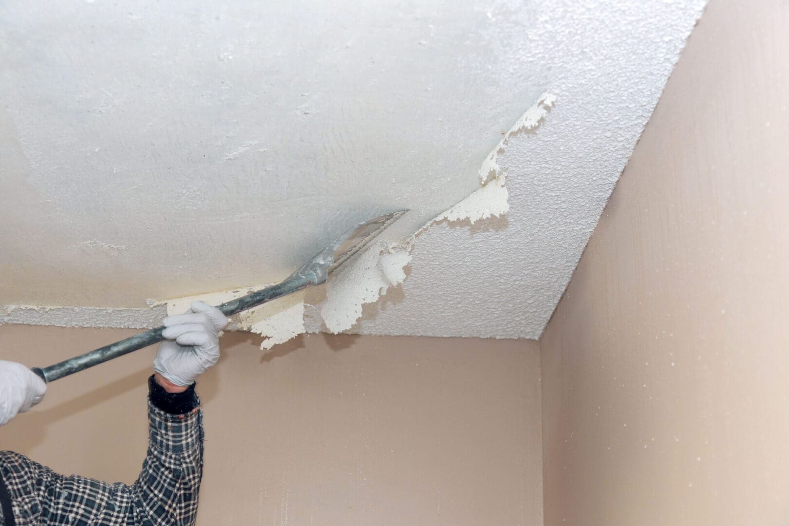Person peeling damaged ceiling paint and drywall.
